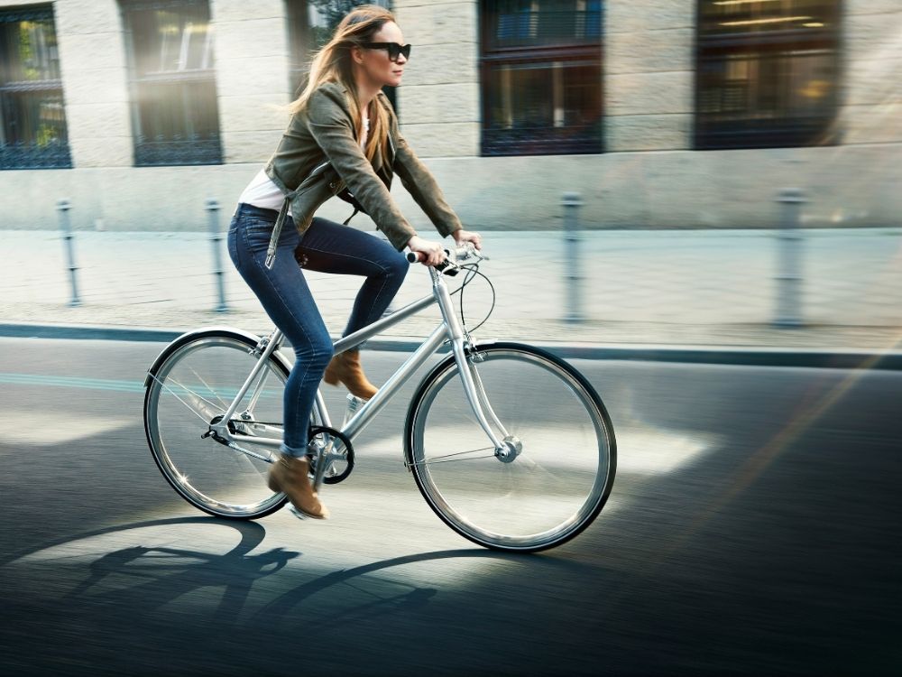A person rides a sleek silver bicycle on a wide urban street, surrounded by blurred motion, suggesting speed and exhilaration.