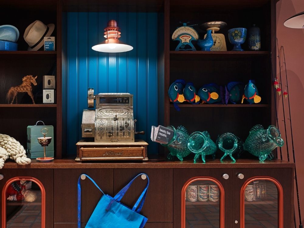 A display featuring a vintage cash register, colorful fish figurines, and assorted collectibles against a blue wall backdrop.