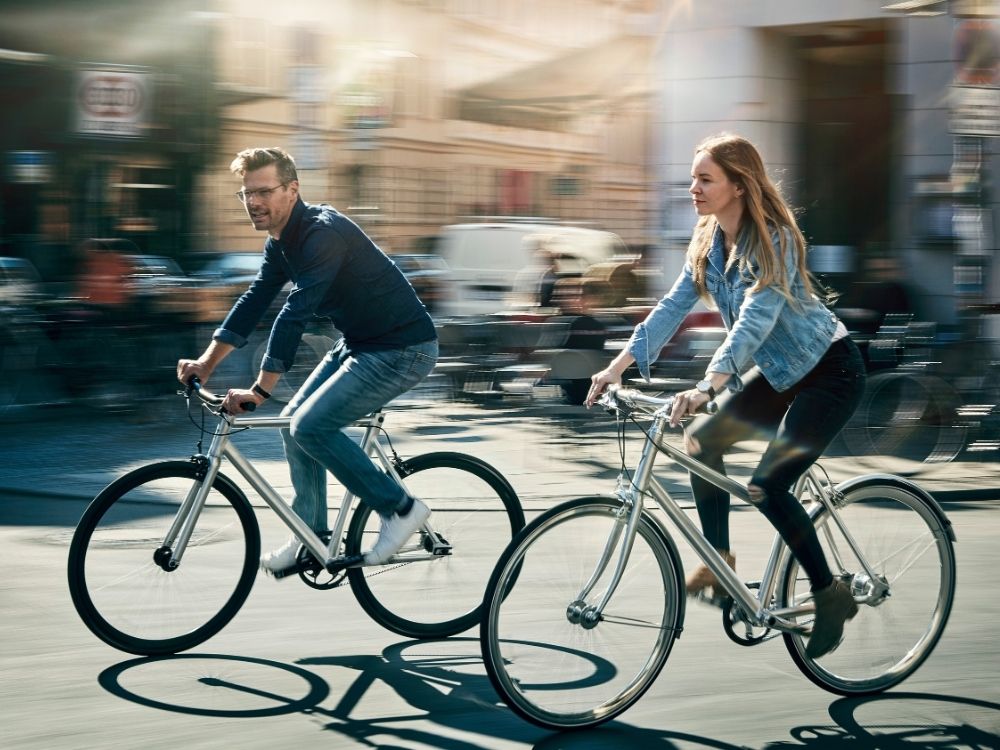 A man and woman joyfully ride bikes on a sunlit city street. Motion blur accentuates their speed and the vibrant, lively urban atmosphere.